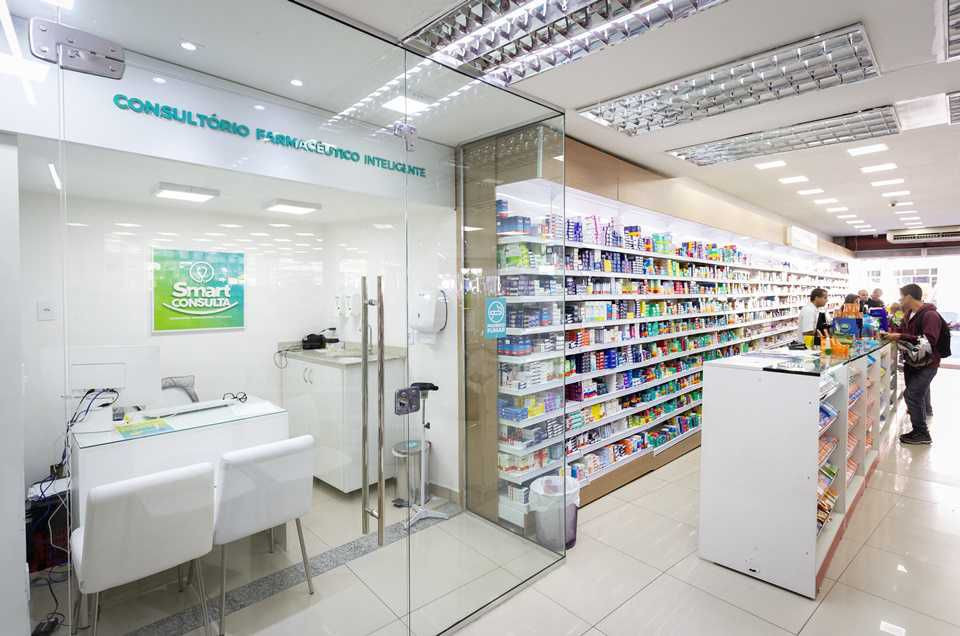 Consultório farmacêutico dentro da farmácia, com mesa de atendimento, cadeiras e equipamentos clínicos em espaço reservado e sinalizado.