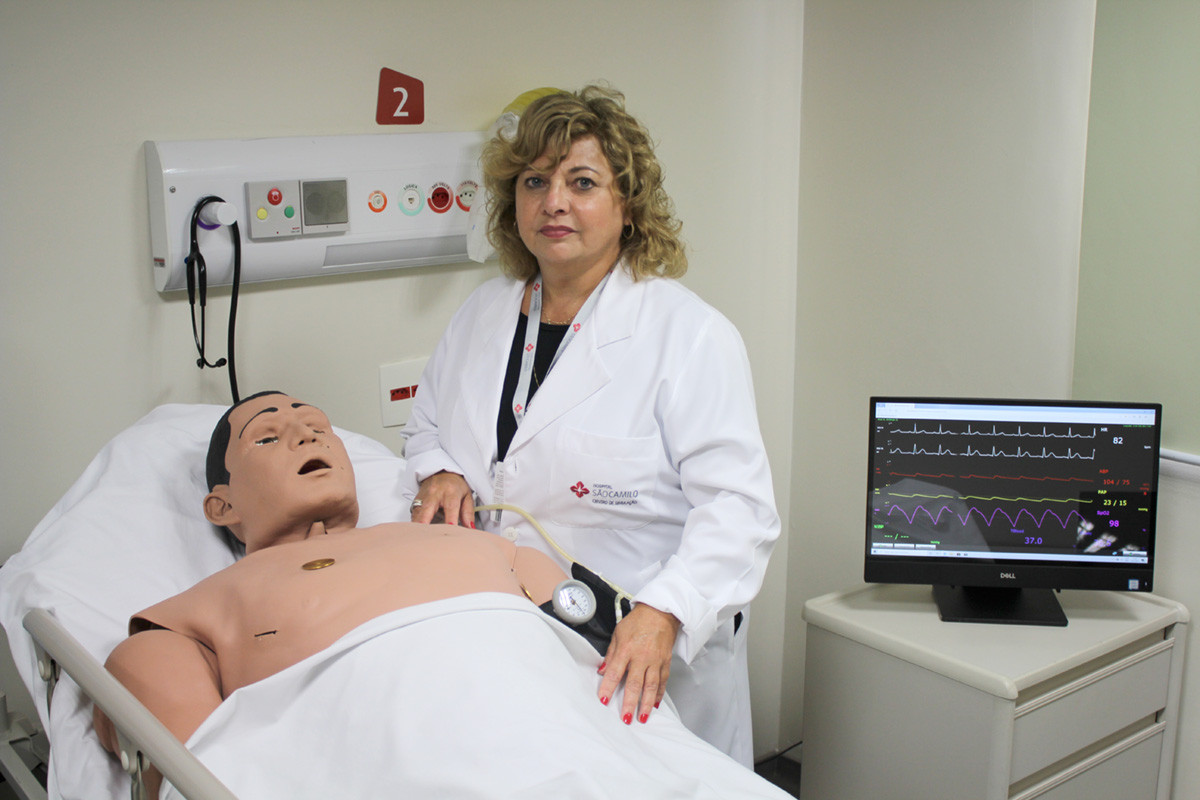 Enfermeira em centro de simulação realística da São Camilo Enfermeira no Centro de Simulação Realística da São Camilo ao lado de manequim de alta fidelidade, com monitor exibindo sinais vitais em tempo real.
