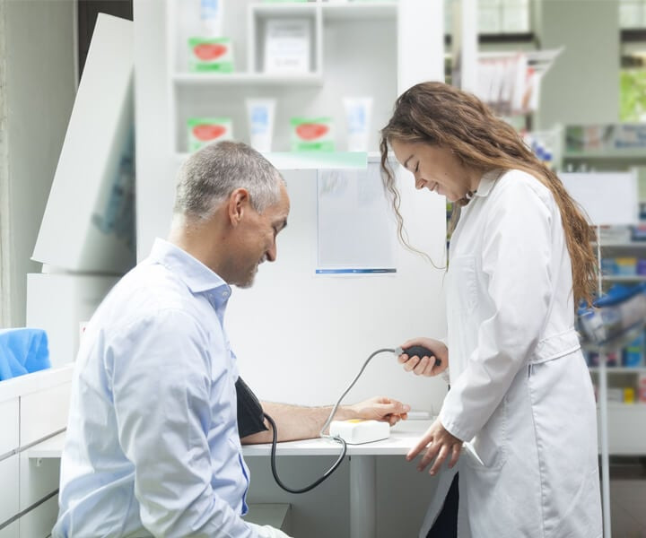 Farmacêutica averiguando a pressão arterial de um paciente em atendimento clínico.