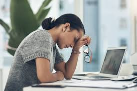 Mulher sentada à mesa de trabalho, apoiando a cabeça sobre a mão e demonstrando sinais de exaustão relacionados ao burnout.
