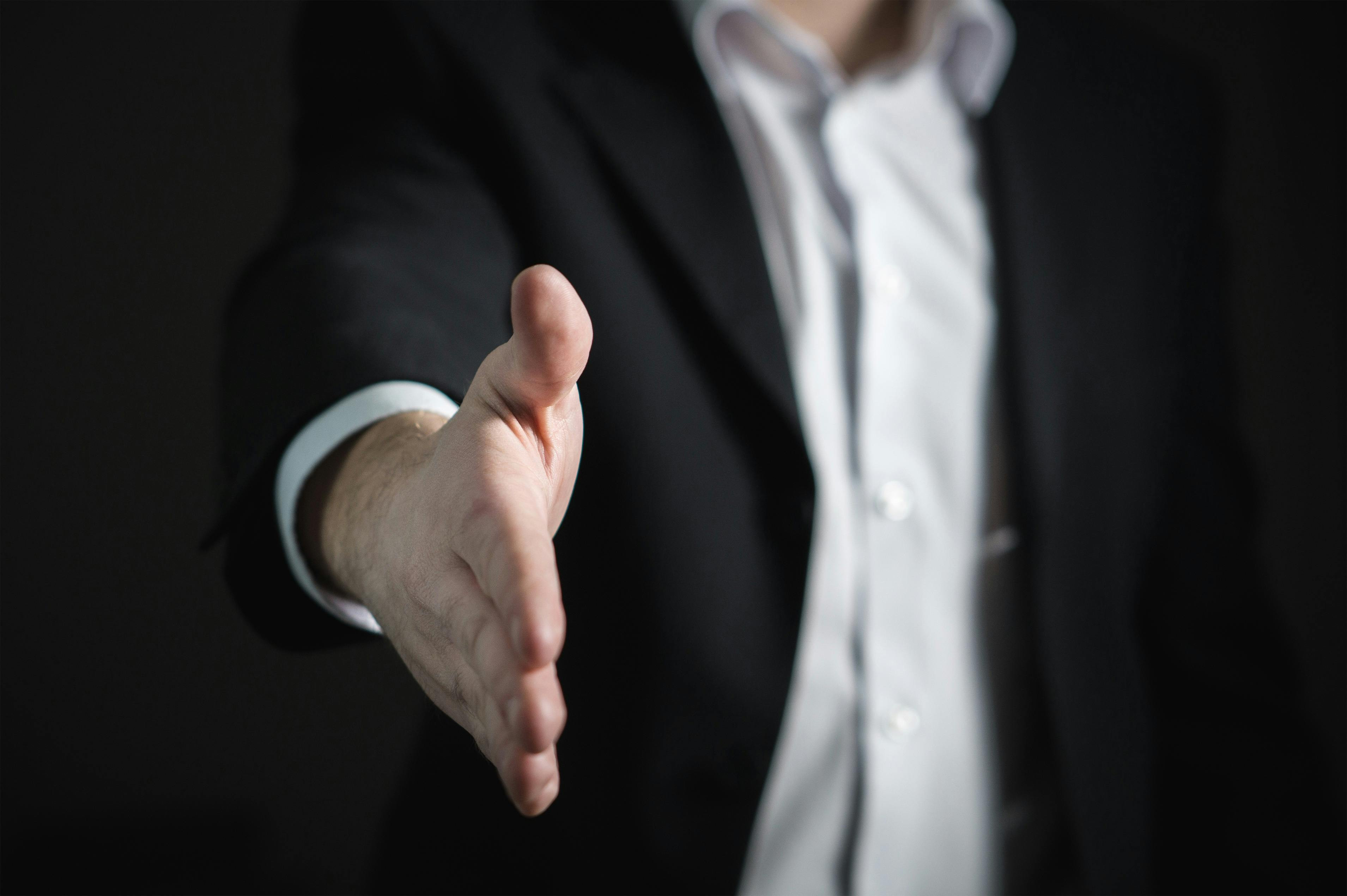 A imagem retrata um profissional estendendo a mão para um aperto, simbolizando boas-vindas, networking, parceria ou uma nova oportunidade de negócios.