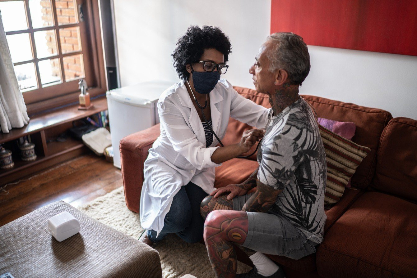 Imagem representativa do acompanhamento domiciliar a pacientes em cuidados paliativos, evidenciando a presença de profissionais da saúde oferecendo suporte clínico e afetivo no ambiente familiar.
