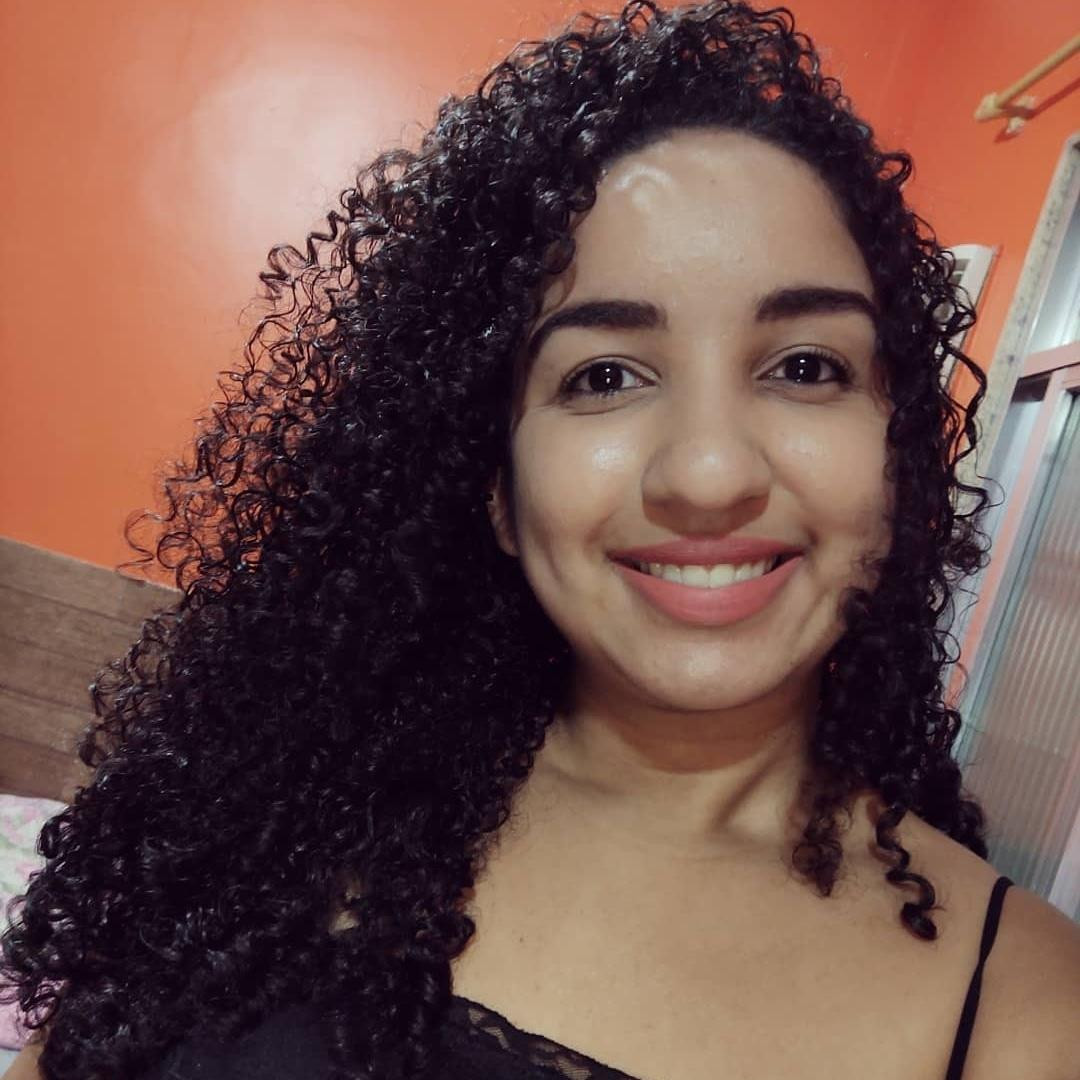 Karen Bastos, aluna da Pós EAD São Camilo, sorrindo levemente em ambiente iluminado, com cabelos soltos e lisos, usando blusa azul escuro.