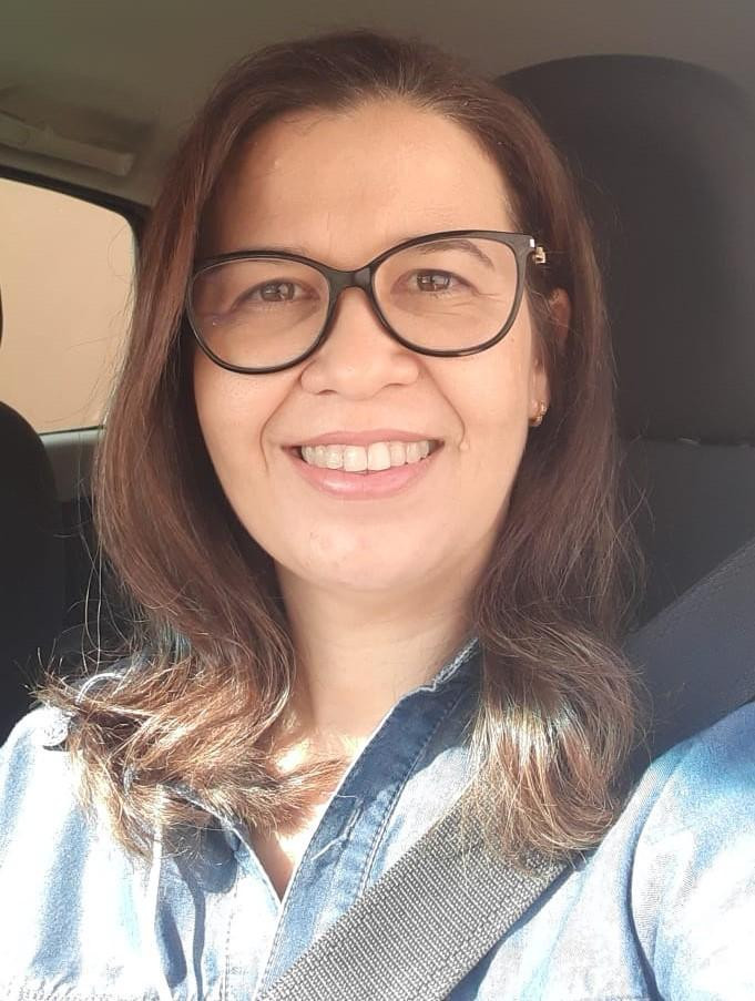 Vanessa Barros, aluna do curso de Pós EAD em Pediatria e UTI Pediátrica e Neonatologia da São Camilo, sorrindo, usando óculos e cinto de segurança, em ambiente interno de um carro.